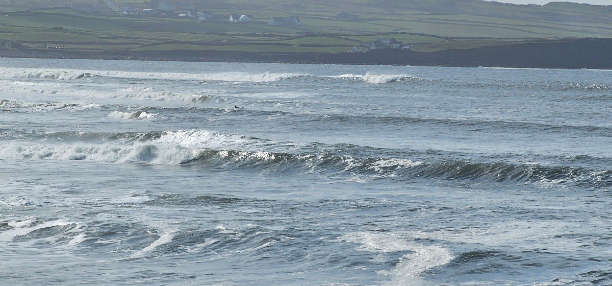 surfer paddling around at Cornish as the sun glistens on the waves